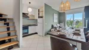 Una cocina moderna con armarios blancos, horno empotrado y comedor con mesa de madera para cuatro comensales.