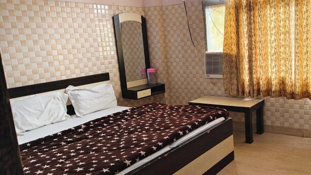 A bedroom with a bed, bedside table, mirror, and curtains. - Vrinda Premium 600m From Prem Mandir (Vrindavan)