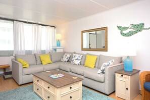 Un salon avec un canapé gris, des coussins jaunes, une table basse en bois, un petit meuble, une lampe et un élément décoratif mural.