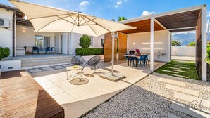 Eine moderne Außenpatio mit überdachter Sitzgruppe, einem kleinen Garten und Blick auf die Berge.