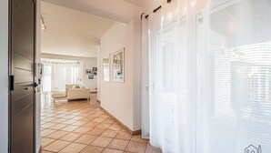 Ein Flur mit Fliesenboden, einer Couch im Hintergrund und einer Tür links.