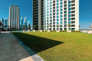 Un edificio moderno con tejado plano y varios balcones, rodeado de una zona verde bien cuidada y un sendero pavimentado.