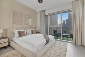 Habitación de hotel moderna con una cama grande, vistas de la ciudad a través de ventanales del suelo al techo y un balcón con mobiliario exterior.