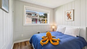 Quarto com uma cama grande, janela com vista para uma casa, quadro na parede e abajur em uma mesa de cabeceira.