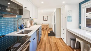 Uma cozinha moderna com armários brancos, painel de fundo azul e piso de madeira.