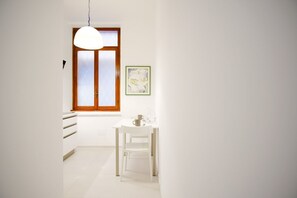 A hallway with a white door, a window with wooden frames, a white table with a chair, and a framed picture on the wall. - Elegantis.it Barberini Modern Apartment (Roma)