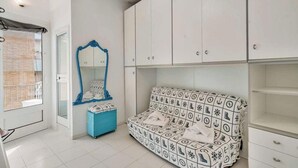 A bedroom with white cabinets, a blue bench, and a patterned sofa. - Welcome to La Goletta, your holiday home on the third and top floor of a quiet building in La Spezia. This cozy two-room apartment is perfect for families, couples or small groups of friends.🛏 Sleeps up to 4 people with a double sofa bed in the living (La Spezia)
