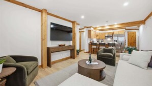 Een moderne woonkamer met een flatscreen televisie, een bank, een salontafel en een keuken op de achtergrond.