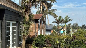 A residential property with a well-maintained lawn, a variety of tropical plants, and a brick house with large windows. - *New Collaroy 3 B/R Northern Beaches Spacious & Renovated Beach Getaway Collaroy (Collaroy)