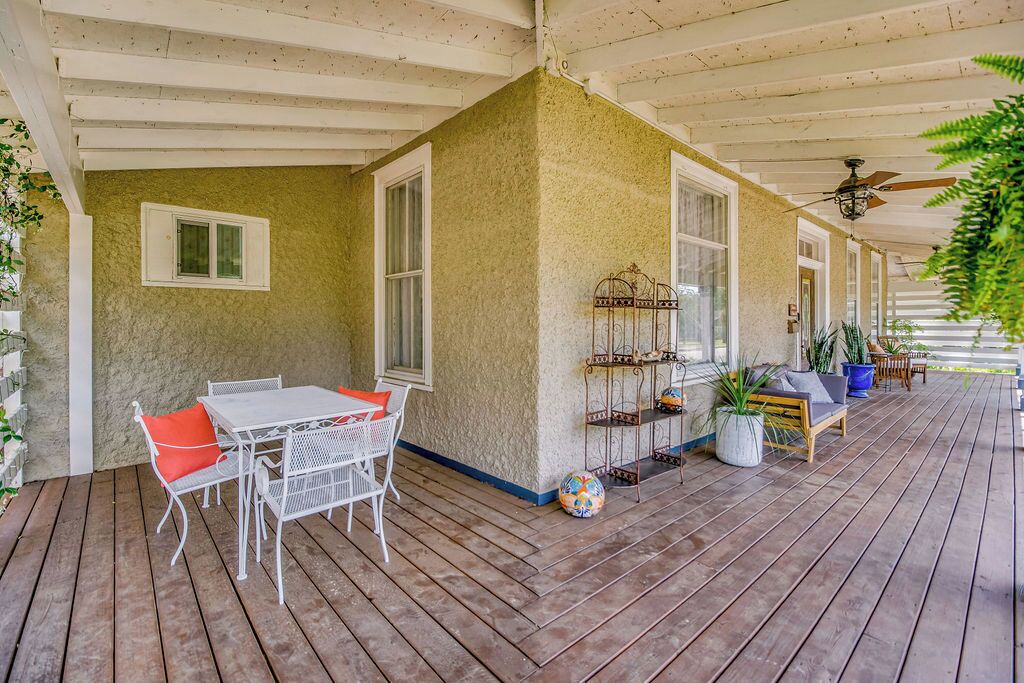 Un patio couvert avec une terrasse en bois, des meubles en métal blanc et des plantes en pot.