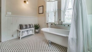 A bathroom with a freestanding bathtub, a white vanity, a shelf with towels, a potted plant, and a wall-mounted light fixture. - Pensacola • 1BR • Sleeps 2 • Close to Downtown (Pensacola)