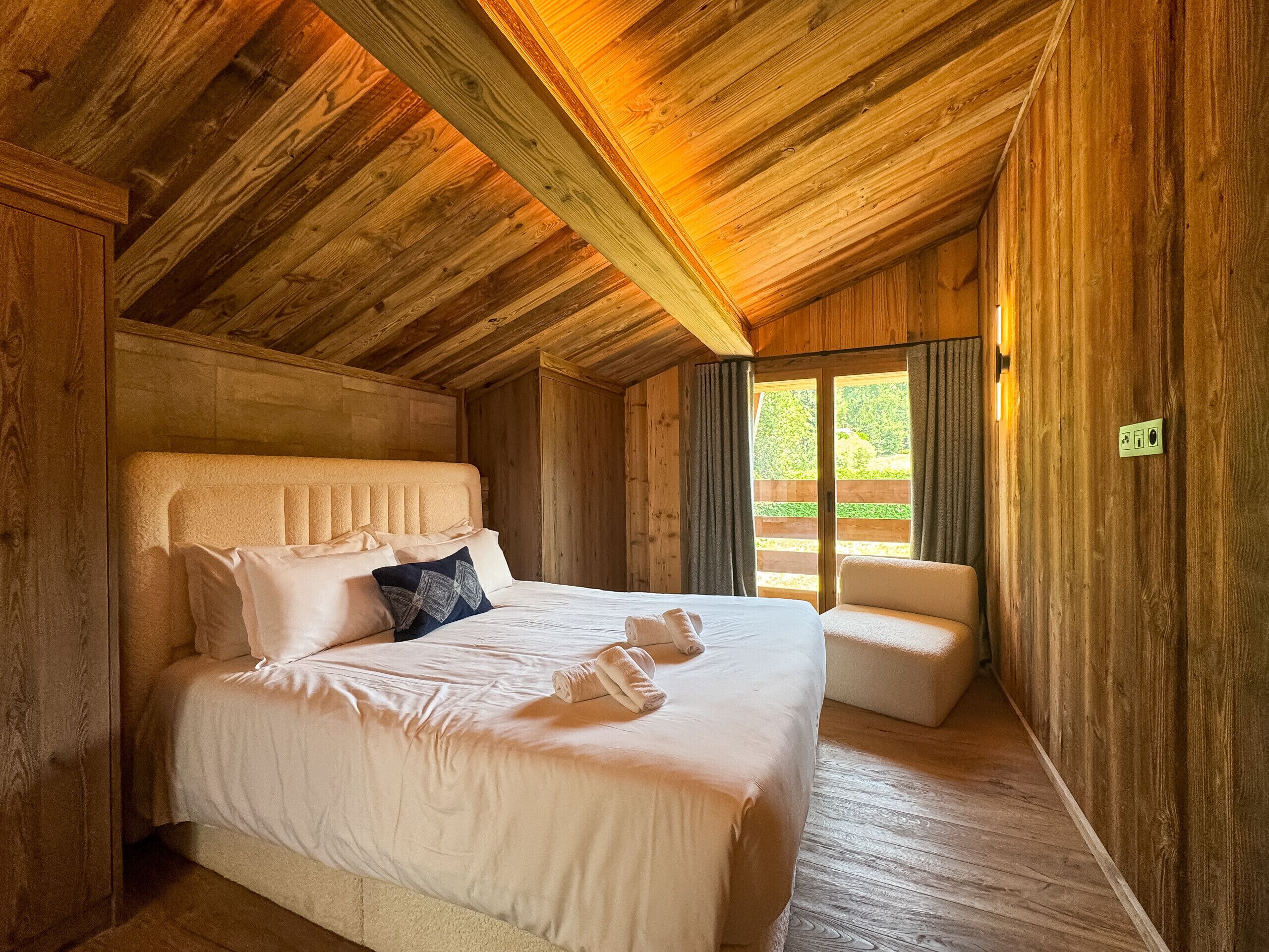 A wooden cabin room with a large bed, a bench, and a sliding door to the outside.