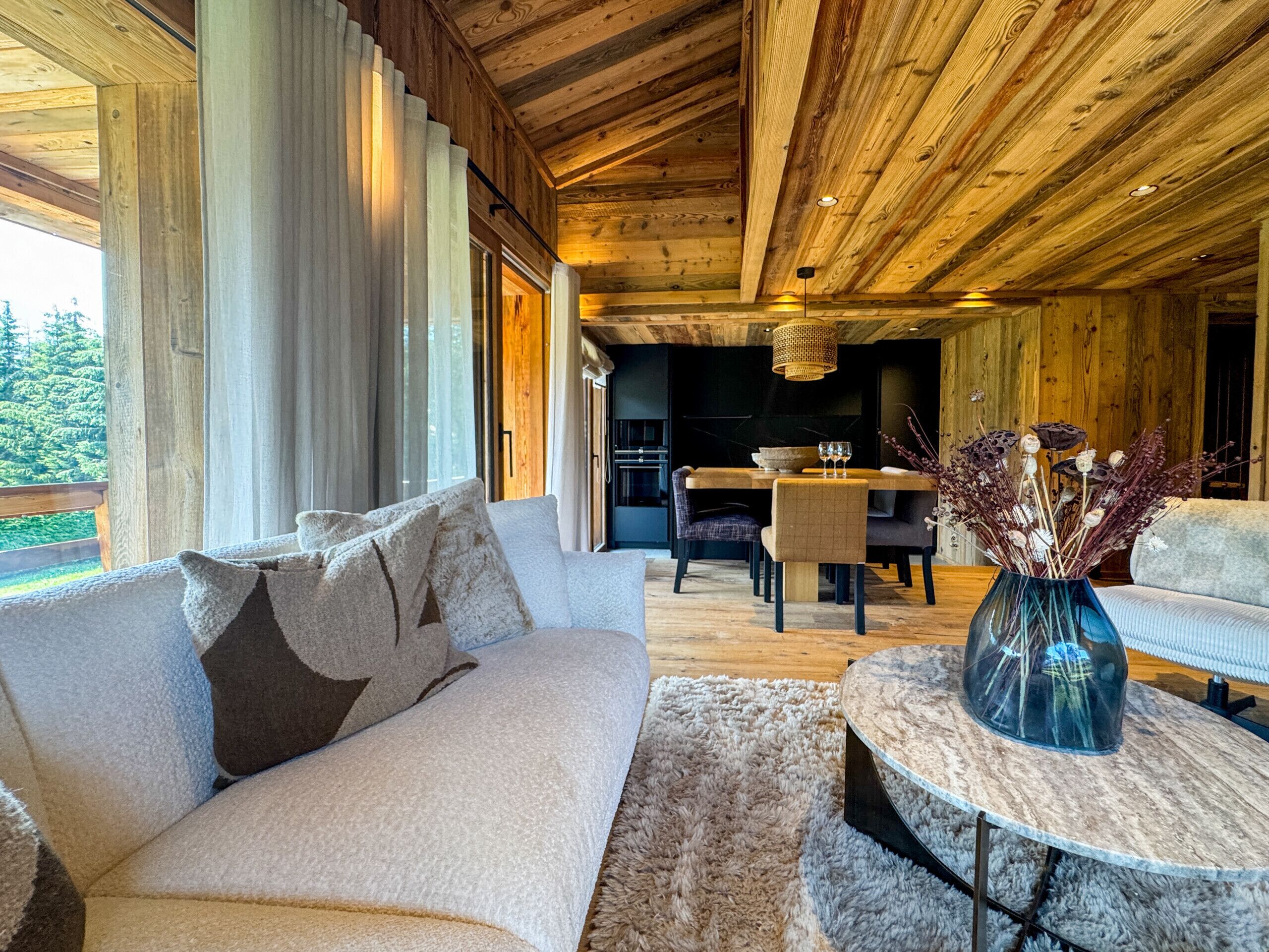 Una habitación acogedora con un sofá, una mesa de comedor y un jarrón con flores secas.