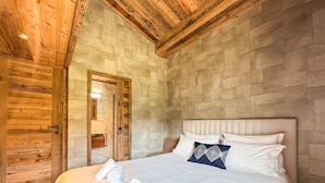 Ein Schlafzimmer mit Holzbalkendecke, Steinwand, einem Bett mit weißer Bettwäsche und einer Holztür.