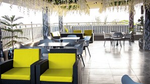A rooftop terrace with wicker furniture, yellow cushions, and hanging white flowers. - Nice-mason Serene and Suites (Benin City)