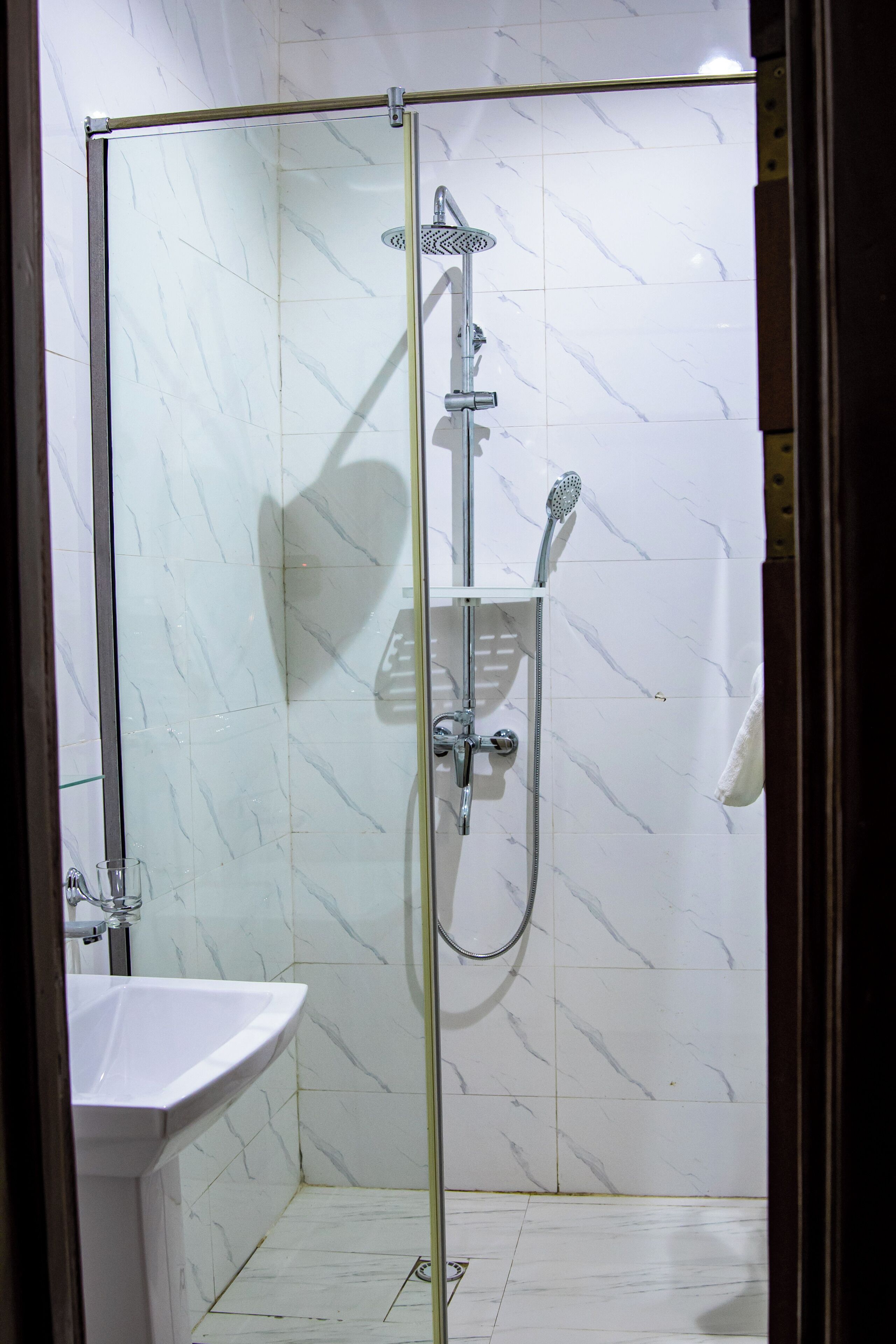 Eine begehbare, gläserne Dusche mit Handbrause und am Wand montiertem Wasserhahn.