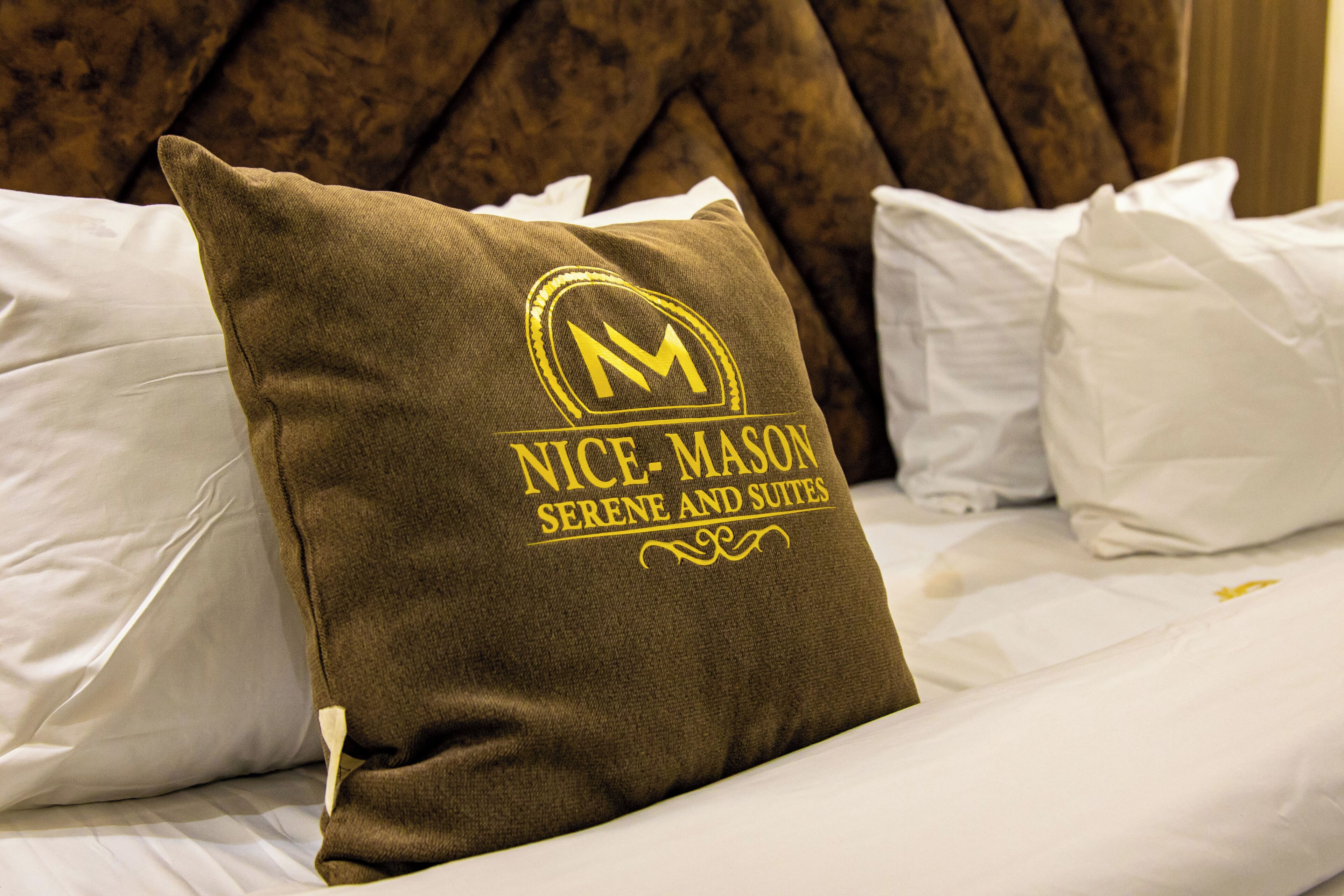 Una cama con un almohadón que muestra el logotipo y el nombre de 'Nice-Mason Serene and Suites'.