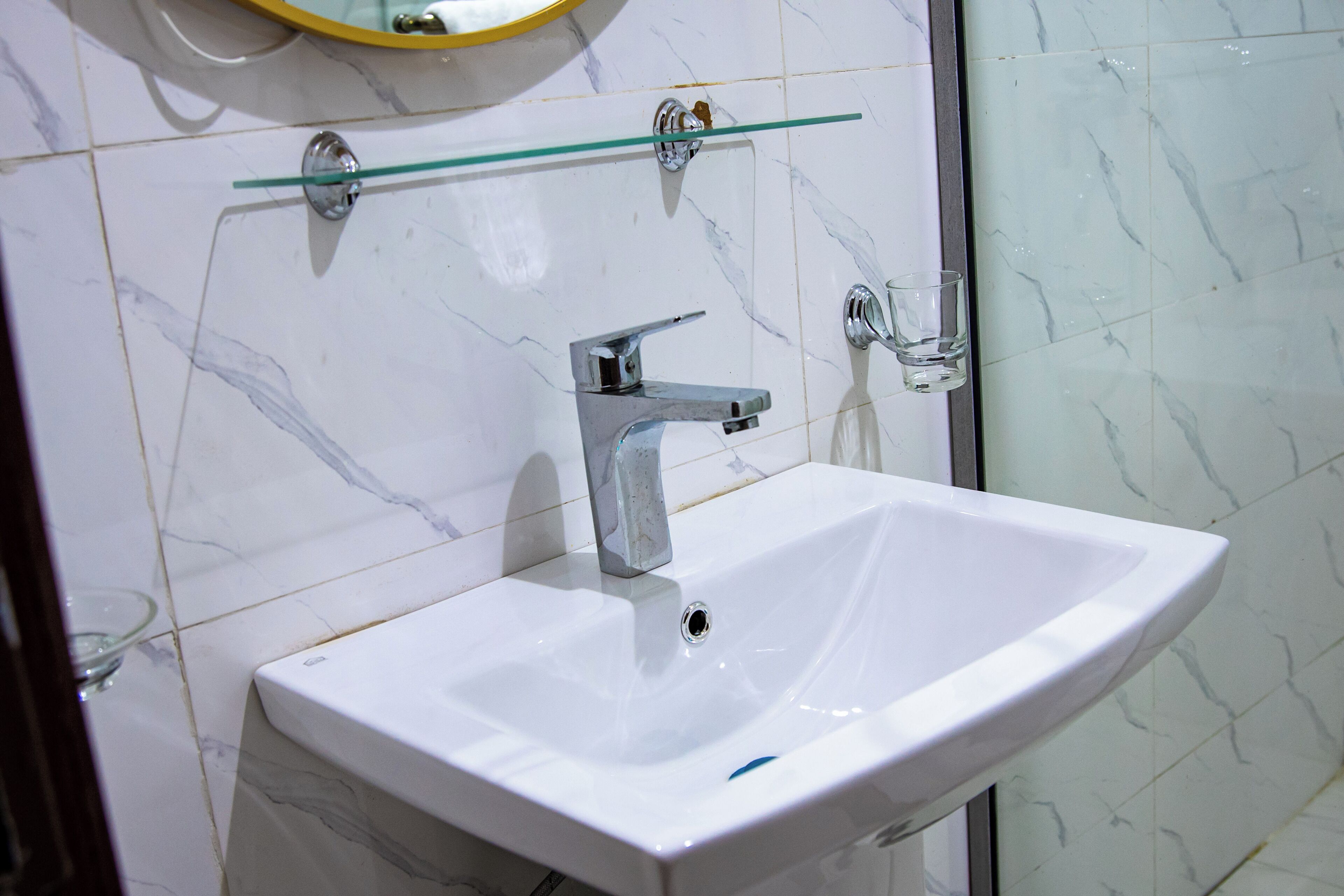 A bathroom with a white sink, a chrome faucet, and a glass shelf above it.