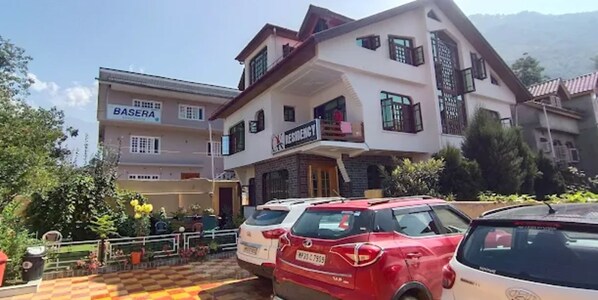 Un edificio de varios pisos con un letrero que dice "BASEERA RESORT". Hay varios coches estacionados frente al edificio.