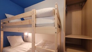 Una cama litera con estructura de madera, ropa de cama blanca y una estantería a la derecha.