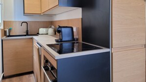 Una cocina compacta con armarios de madera, encimera negra, horno empotrado, tostadora y hervidor.