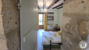 Ein schmales Gang, der in ein Schlafzimmer mit einem Bett, einem Sessel und einem Bücherregal führt.