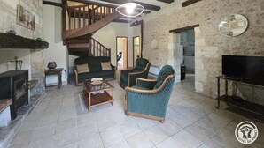 Ein rustikales Wohnzimmer mit freiliegenden Holzbalken, einem Kamin und einer Treppe, die zu einer oberen Ebene führt.