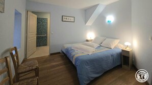 A bedroom with a bed, bedside lamps, a wooden chair, and a door leading to another room. - Périgord Cottage with Garden, WIFI & Pets Welcome (Sorges et Ligueux en Périgord)