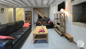A modern living room with a black leather sofa, a wooden coffee table, and a wooden bookshelf. - Périgord Cottage with Garden, WIFI & Pets Welcome (Sorges et Ligueux en Périgord)