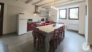A kitchen with a dining area, featuring a large table and chairs, a refrigerator, and cabinets. - Périgord Cottage with Garden, WIFI & Pets Welcome (Sorges et Ligueux en Périgord)