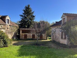 A courtyard with stone buildings, a large tree, and a grassy area.
