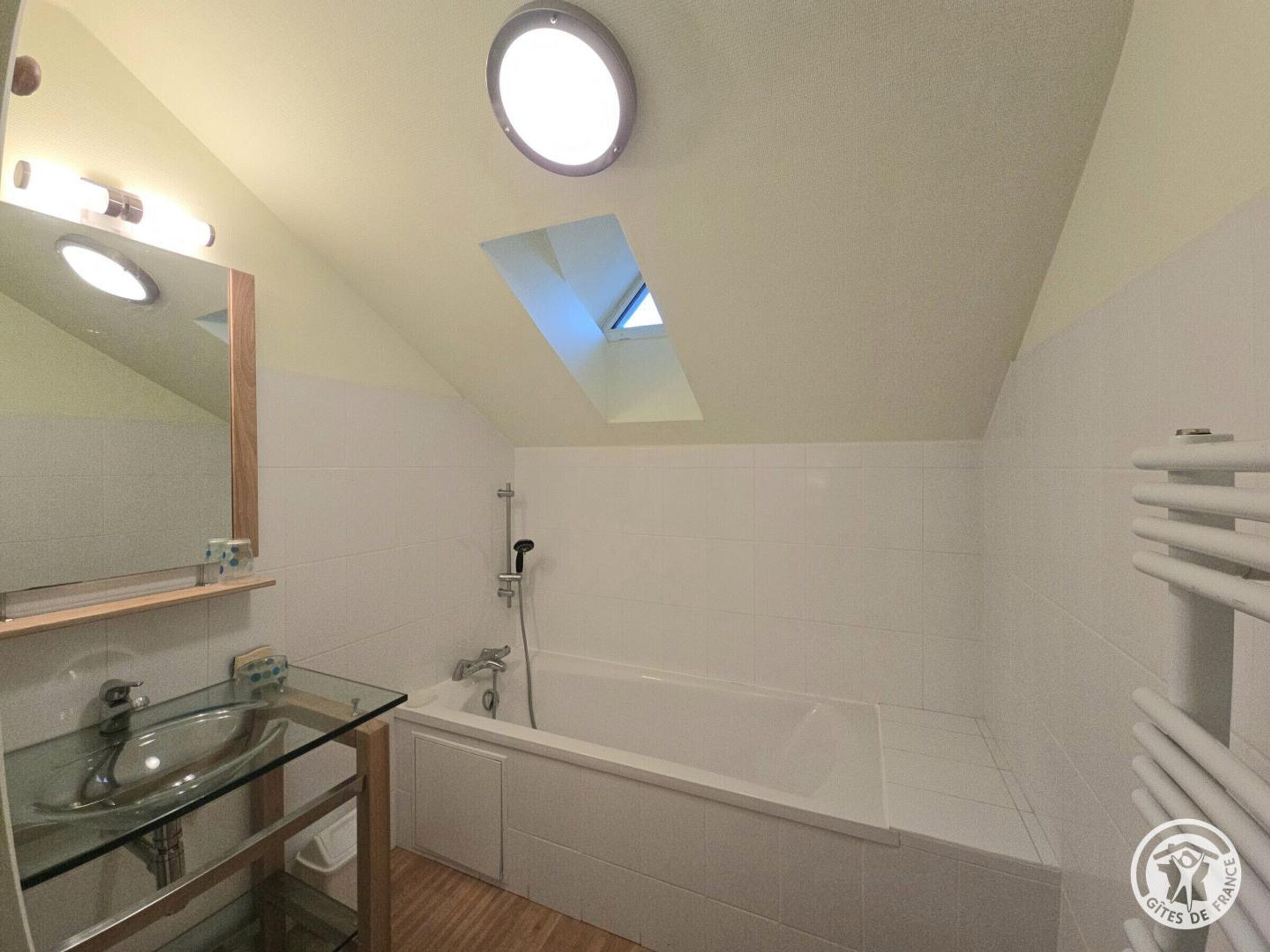 A modern bathroom with a glass sink, a large bathtub, and a skylight.