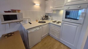 A compact kitchen with white cabinetry, a microwave, a sink, and an oven.