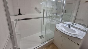 A modern bathroom with a glass shower enclosure, a white sink with a marble countertop, and a large mirror above the sink.
