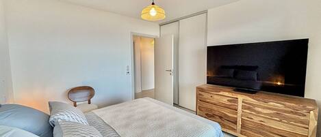A modern bedroom with a bed, a TV on a wooden cabinet, and a hanging light fixture.