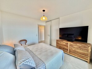 A modern bedroom with a bed, a TV on a wooden cabinet, and a hanging light fixture. - Porticcio: 3-Room Apartment with Sea View, Parking, 4 Pax (Porticcio)