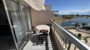 Ein Balkon mit Tisch und Stühlen, der Blick auf ein Gewässer und einen Strand bietet.