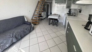 Eine kompakte Küche mit eingebautem Herd, ein Essbereich mit einem kleinen Tisch und ein graues Sofa.