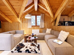 Ein gemütliches Blockhaushaus-Interieur mit Holzbalkendecke, einer Couch, einem Couchtisch und einem Teppich.