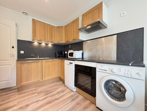 A compact kitchen with wooden cabinets, a built-in microwave, a dishwasher, and a washing machine. - Comfortable T3 in Mont-Dore with WiFi (Mont-Dore)