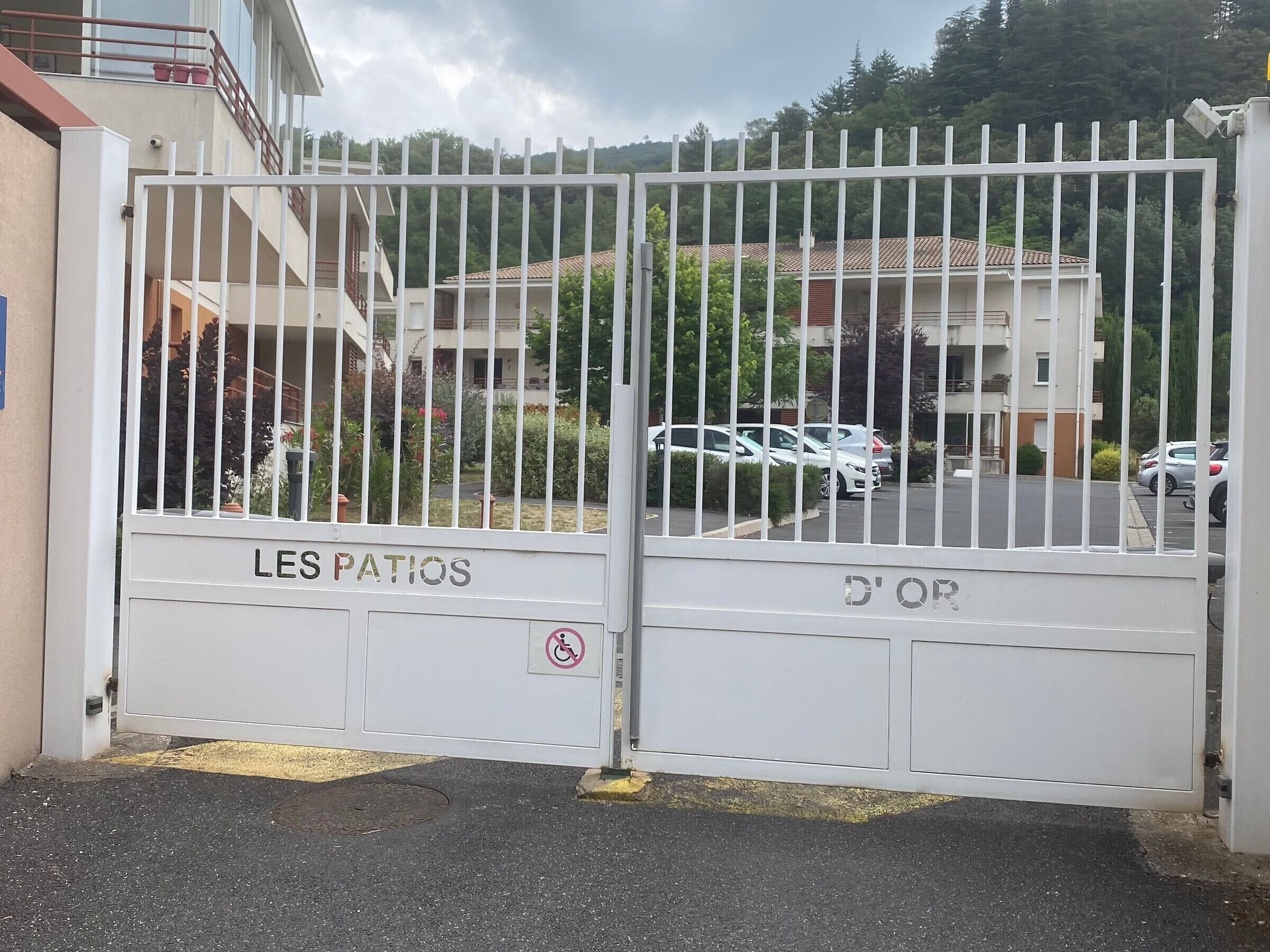 A gated entrance to a residential area with a sign reading 'LES PATRIOS' and a disabled parking symbol.