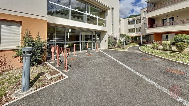 Un edificio moderno con amplios ventanales, un patio empedrado y un jardín bien cuidado.