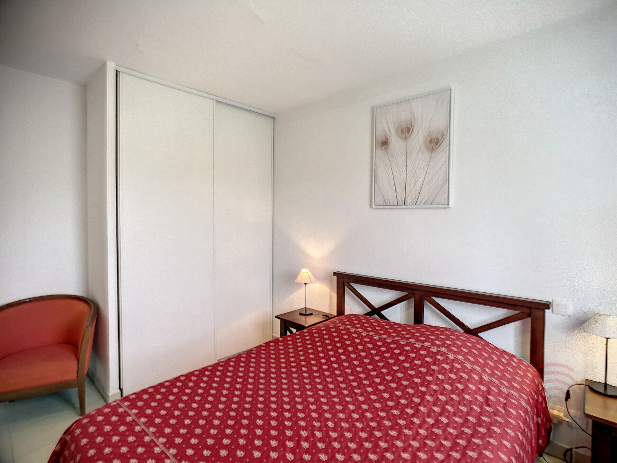 Ein Schlafzimmer mit einem Bett, einem Sessel, einem Nachttisch mit Lampe und einem Kleiderschrank.