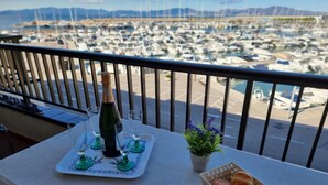 Un balcon avec une table dressée pour un repas, une bouteille de champagne et une vue sur une marina remplie de bateaux.