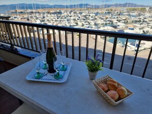 A balcony with a table set for a meal, a bottle of champagne, and a view of a marina with boats. - Cozy apartment in L'Escala with terrace near the beach (L'Escala)