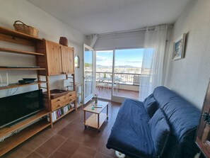 A living room with a sofa, a TV, wooden shelves, a small table, and a balcony with a view. - Cozy apartment in L'Escala with terrace near the beach (L'Escala)