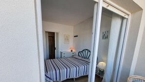 Une chambre à coucher comprenant un lit, une table de chevet, une lampe, une chaise et une porte-fenêtre coulissante donnant sur un balcon.