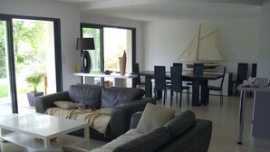 Una sala moderna con sofá, una mesa de centro y un comedor con sillas y una maqueta de un velero.