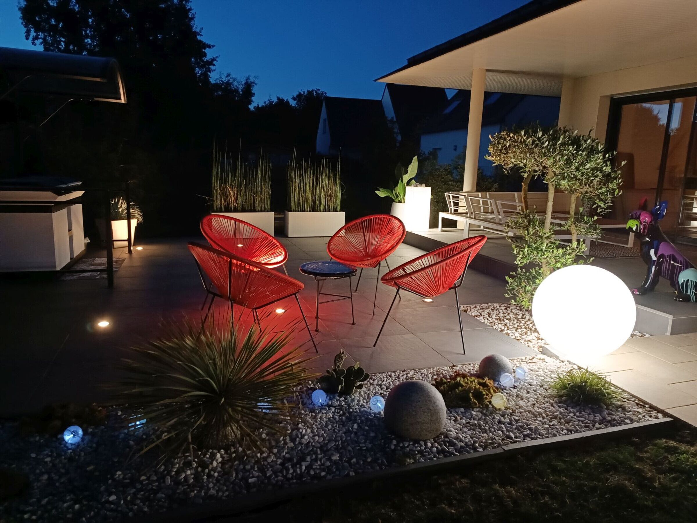 An outdoor patio area with red chairs, a round table, and a decorative light.