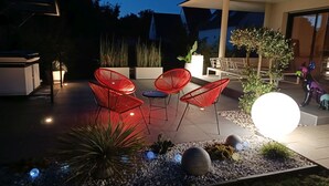 Un patio al aire libre con sillas rojas, una mesa redonda y una lámpara decorativa.